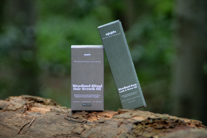 The Woodland Pair: Woodland Ritual Hair Growth Oil and Woodland Gaze lash and brow oil boxes on a forest log