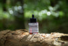 Woodland Ritual Hair Growth Oil, 50ml amber dropper bottle, on a log in a sunlit forest
