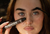 Woman holding Woodland Gaze lash and brow growth oil while brushing it through her brows
