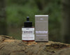 Woodland Ritual Hair Growth Oil dropper bottle beside its box on a forest log